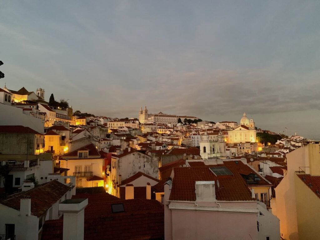 Alfama’s terracotta rooftops at dusk from Miradouro das Portas do Sol, with São Vicente de Fora and the National Pantheon lit up behind