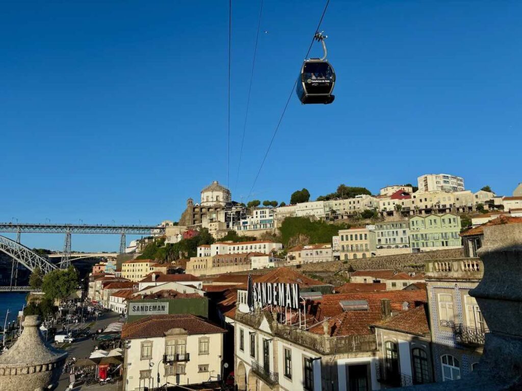 Gaia cable car passing above the Sandeman port cellars in Vila Nova de Gaia, with Dom Luís I Bridge and the Serra do Pilar monastery behind