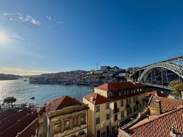 View across the Douro from the Gaia side to Porto’s Ribeira waterfront and the Dom Luís I Bridge on a sunny afternoon, terracotta roofs in front